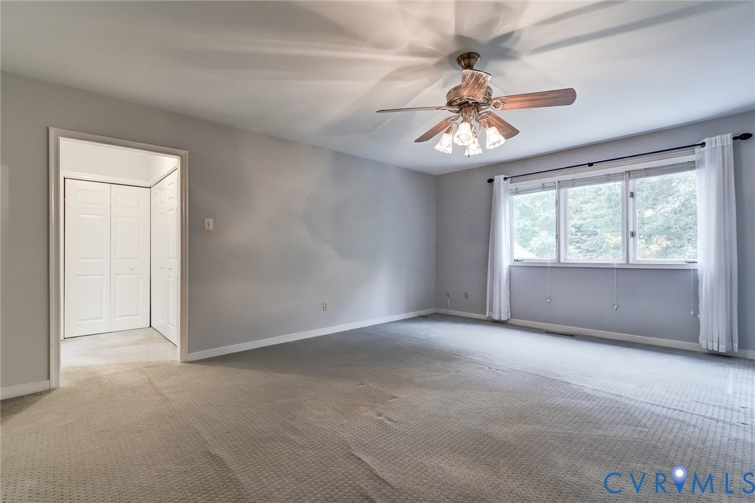 Neutral interior space featuring wall-to-wall carpeting, a multi-pane window with a curtain rod, a ceiling fan with integrated lighting, and a closet with bifold doors