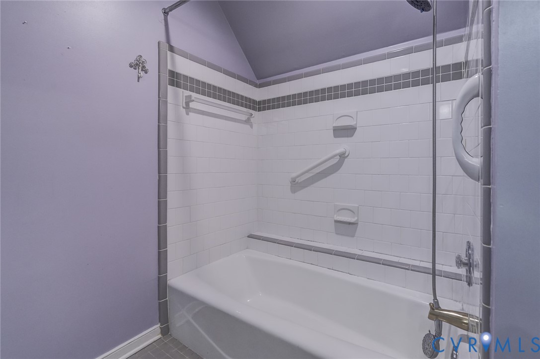 Bathtub surround featuring white subway tile, a gray accent border, built-in soap dishes, a mounted grab bar, and a handheld shower fixture