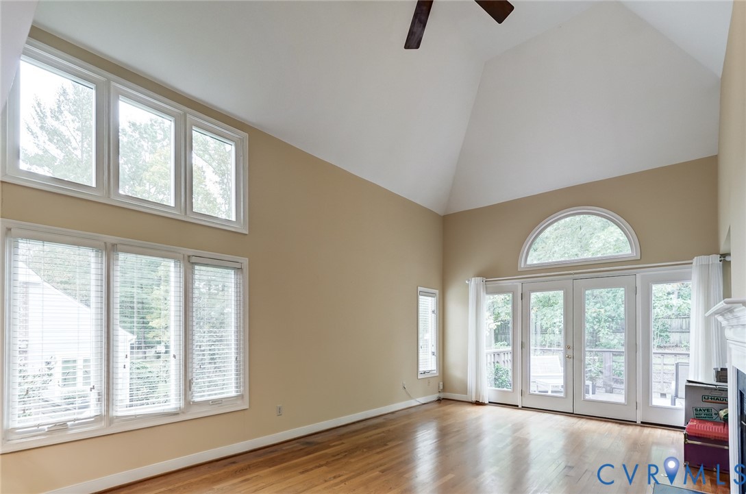 Vaulted ceilings featuring a built-in ceiling fan, oversized multi-pane windows, arched transom window, wood-finish flooring, and double glass-pane doors