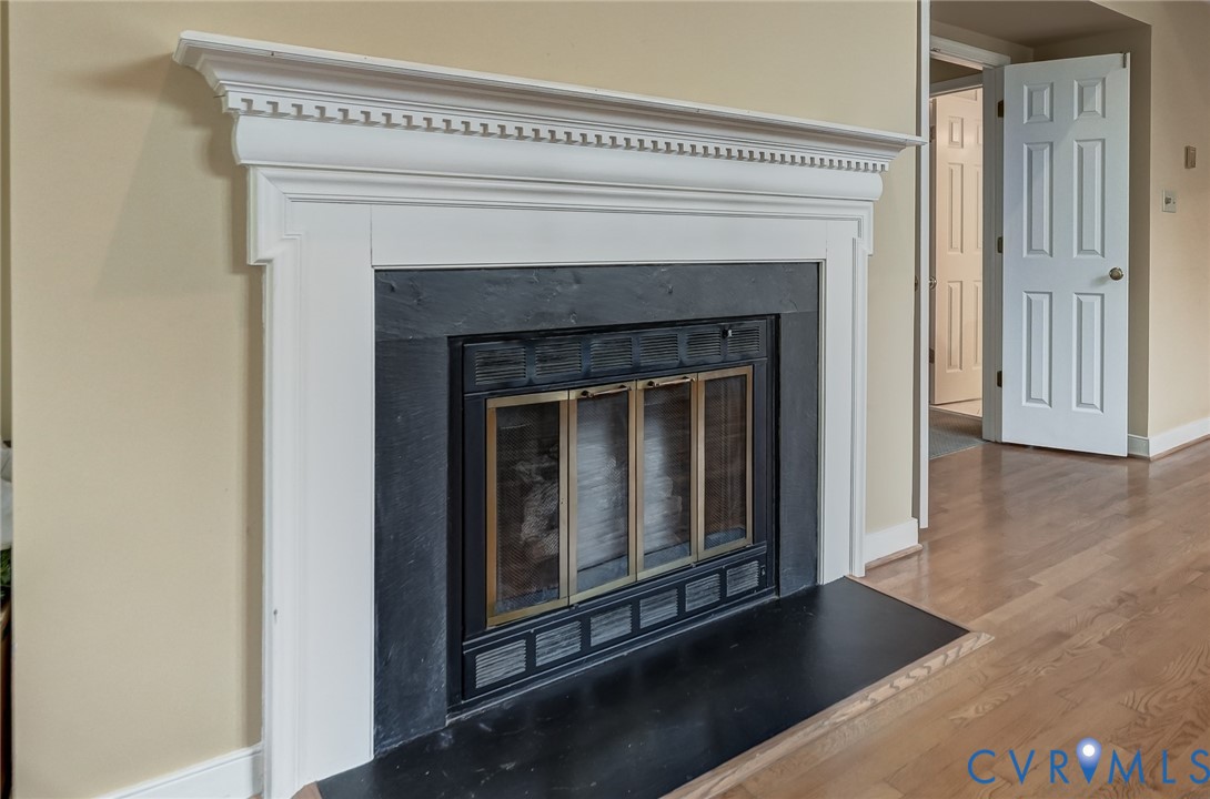 Fireplace featuring a white decorative mantel, dark stone surround, black hearth, and wood-finish flooring