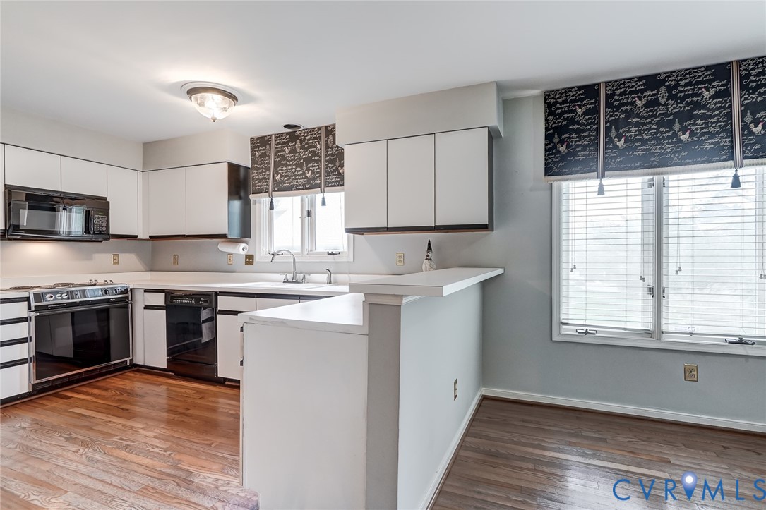 Kitchen featuring white flat-panel cabinetry, a peninsula with a raised counter, wood-finish flooring, and built-in black appliances