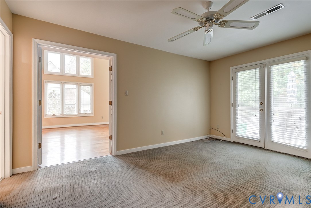 Room featuring white-framed double doors, glass-paneled exterior doors, a ceiling fan, and window-lined walls