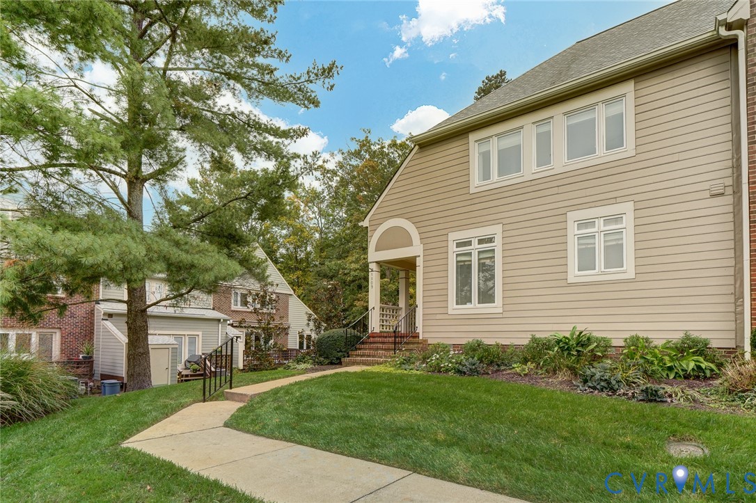 Exterior featuring beige horizontal siding, multi-paned windows, a covered entryway with an arched detail, and a concrete walkway bordered by established greenery