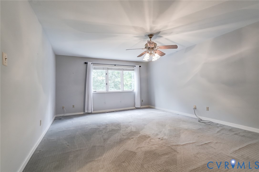 Neutral-toned interior space featuring wall-to-wall carpeting, a multi-pane window with trim, and a ceiling-mounted light fixture with a central fan