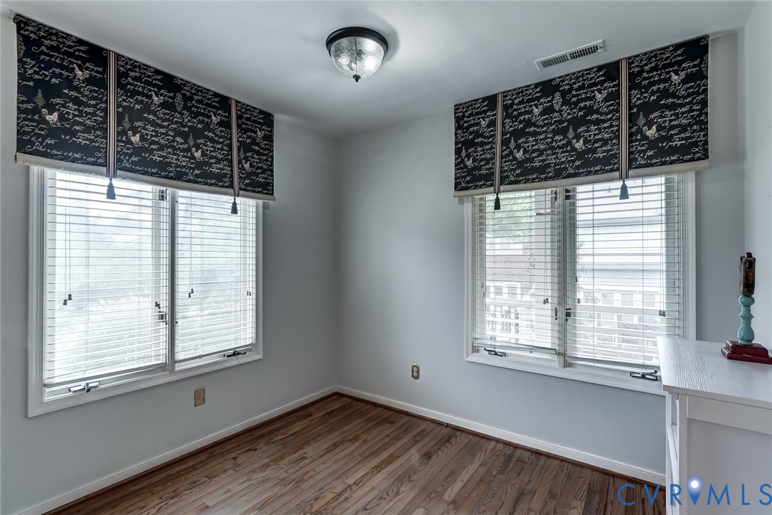 Room featuring wood-finish flooring, two windows with horizontal blinds, and a central ceiling-mounted light fixture