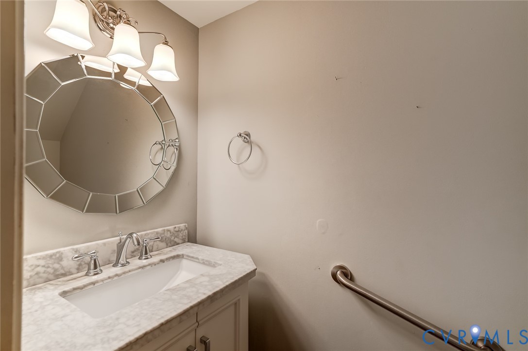 Vanity featuring a stone-composite countertop with an integrated rectangular basin, three-light polished chrome fixture, decorative circular multi-faceted mirror, and metal wall-mounted grab bar