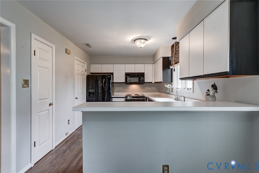Kitchen featuring white cabinetry, a breakfast bar with a solid surface countertop, wood-finish flooring, and integrated black appliances including an over-the-range microwave