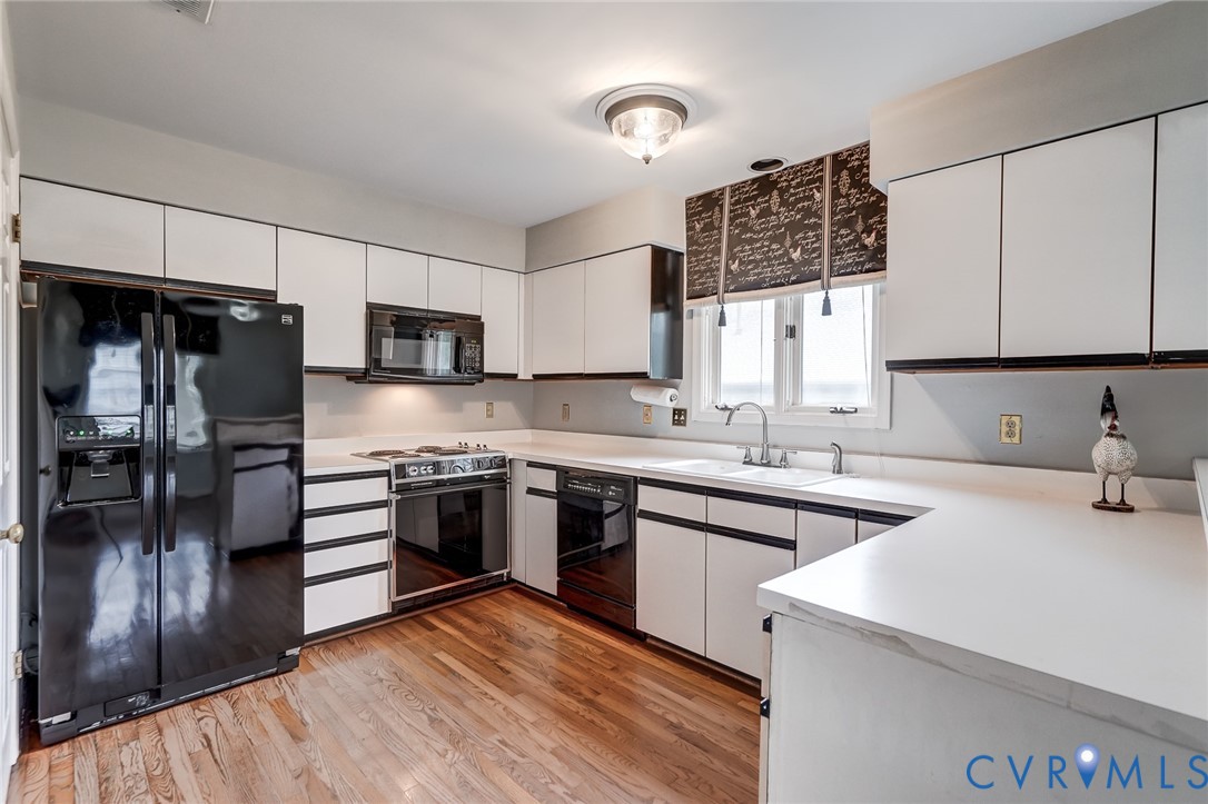 Kitchen featuring white cabinetry with black trim, wood-finish flooring, integrated black appliances, and white solid-surface countertops