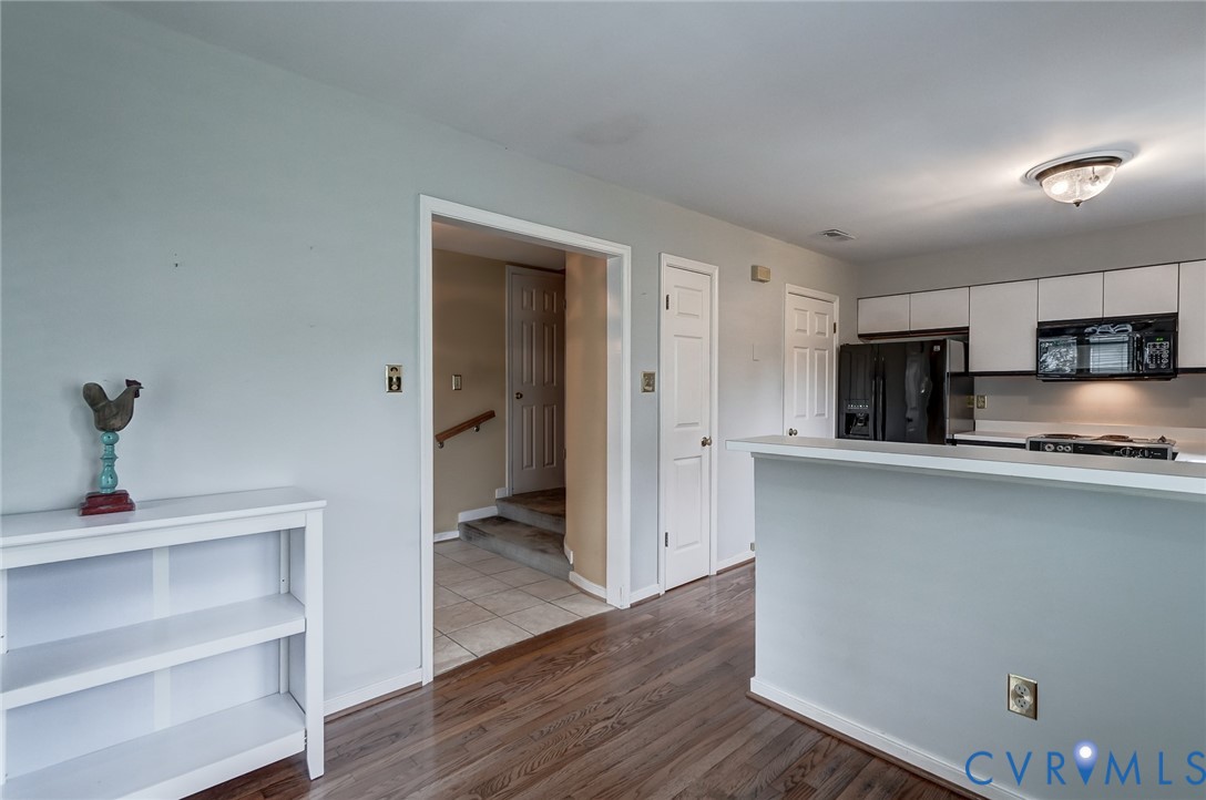 Kitchen featuring a breakfast bar, white cabinetry, dark-finish appliances, wood-finish flooring, and a flush-mount ceiling light