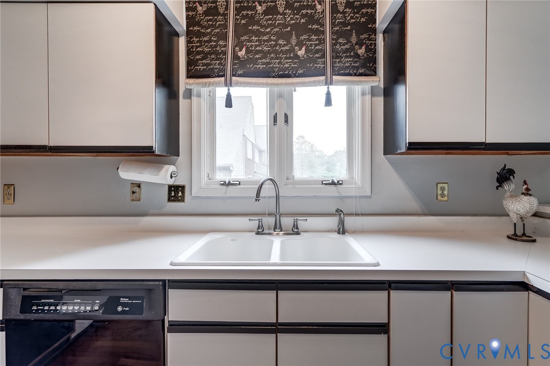 Kitchen featuring white cabinetry with dark trim, white countertops, integrated double-basin sink with metallic faucet, and a built-in dishwasher