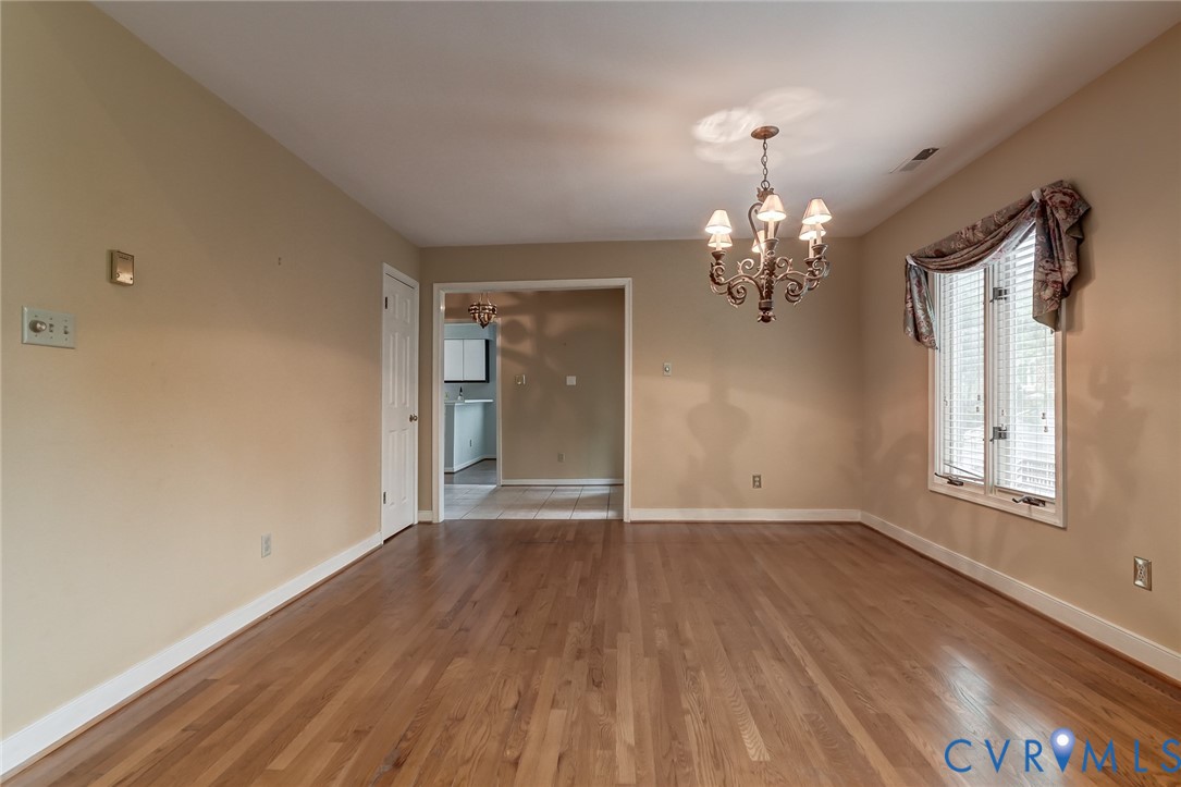 Dining area featuring wood-finish flooring, a multi-arm decorative chandelier, and a window with horizontal blinds