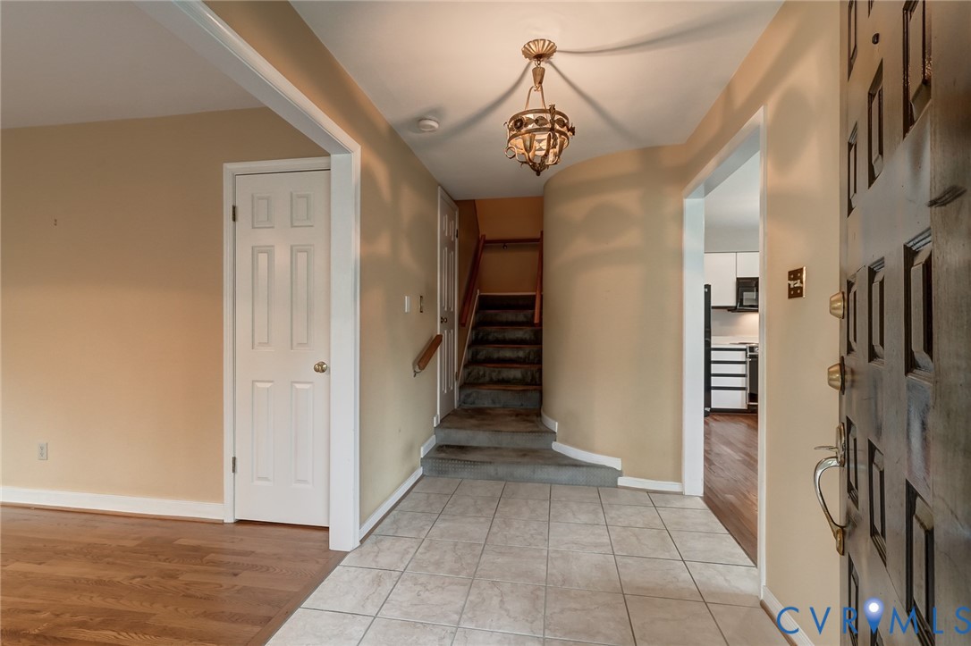 Entryway featuring a decorative hanging light fixture, tile flooring, wood-finish flooring, a paneled door, and a staircase with a wooden handrail