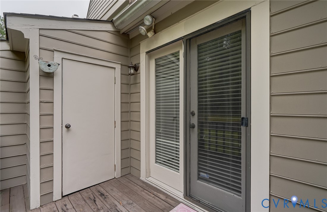 Exterior entryway featuring horizontal lap siding, a dedicated storage closet, integrated security lighting, and a glass-panel door with a screened storm door