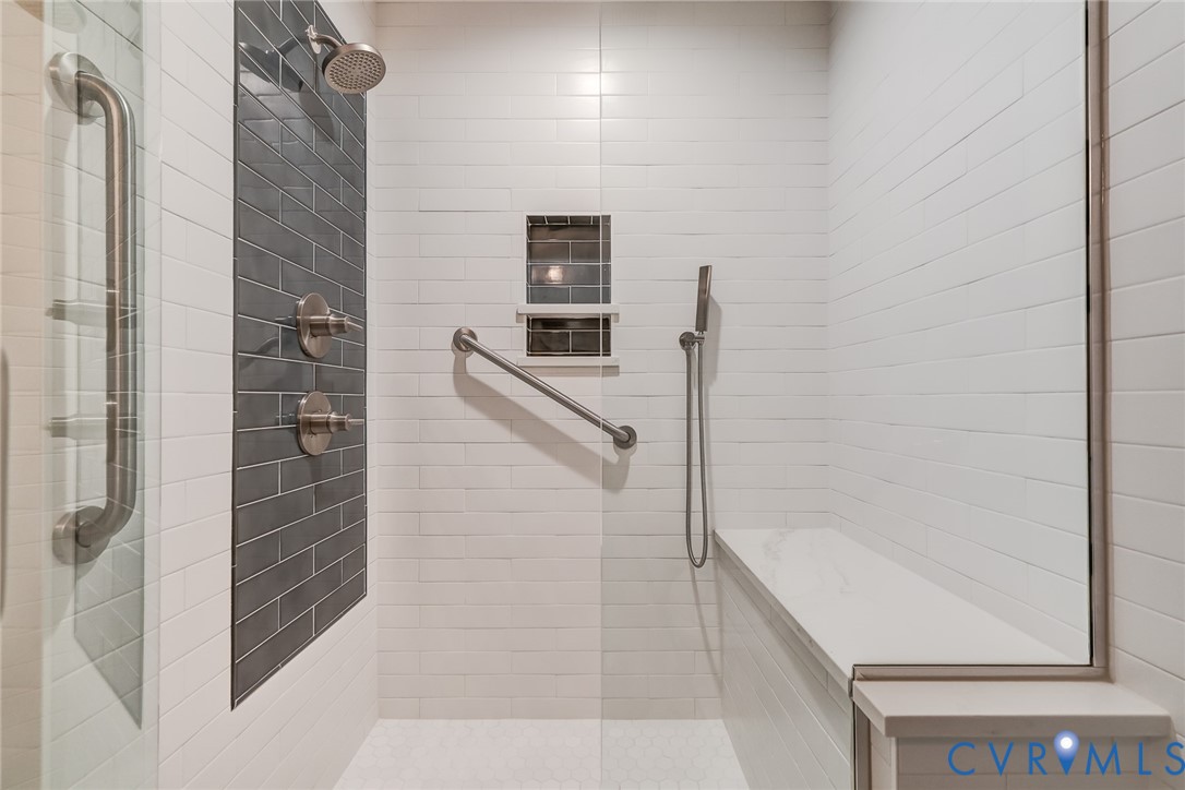 Walk-in shower featuring white subway wall tile, a dark-toned tiled accent panel, a built-in bench, a wall-mounted hand shower, and brushed-finish fixtures