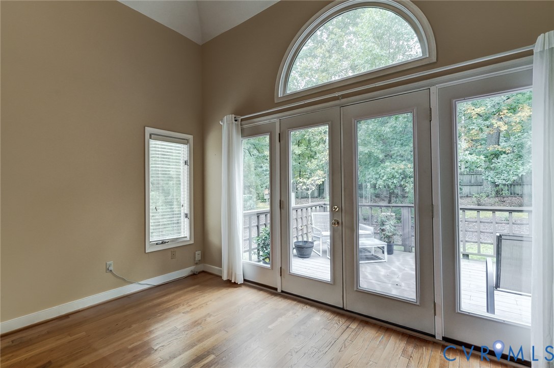 Vaulted ceilings, wood-finish flooring, double glass doors with a half-moon window, and a wood deck