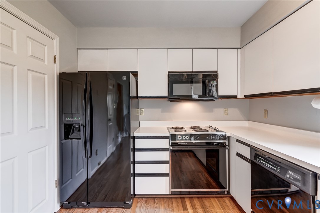 Kitchen featuring white cabinetry with black trim, solid-surface countertops, wood-finish flooring, and black appliances including a range, microwave, and refrigerator