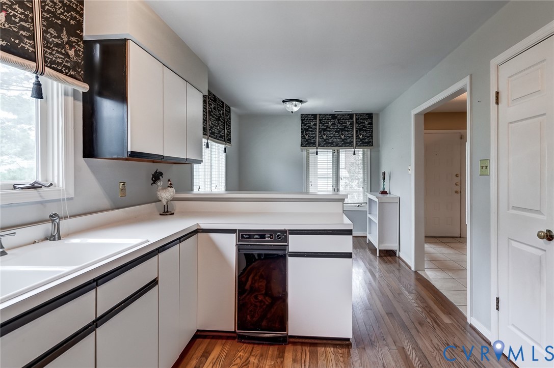 Kitchen featuring cabinetry with contrasting trim, solid surface countertops, built-in dishwasher, and wood-finish flooring