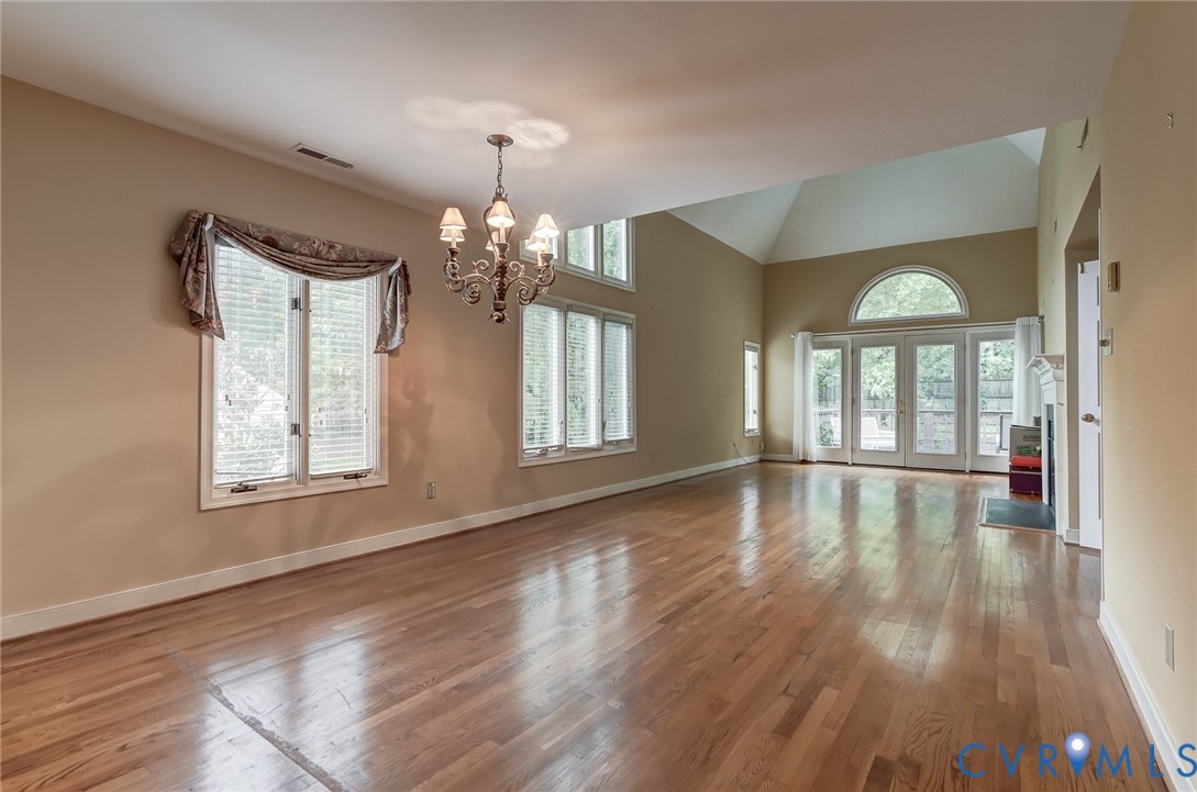 Vaulted ceilings, wood-finish flooring, multi-pane windows, a decorative chandelier, and double French doors with a semi-circular transom