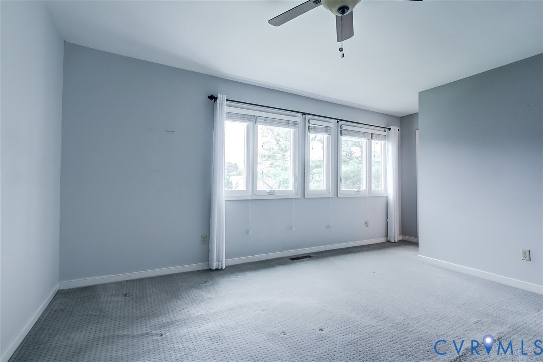 Spacious room featuring neutral carpeting, triple-window configuration with white trim, and a ceiling-mounted fan