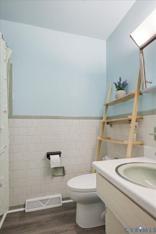 Bathroom featuring white rectangular wall tile with green bullnose trim, wood-finish flooring, a vanity with a solid-surface countertop and integrated sink, and an attached medicine cabinet