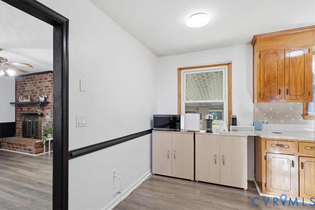 Kitchen featuring natural wood cabinetry, wood-finish flooring, and a red brick fireplace in the background