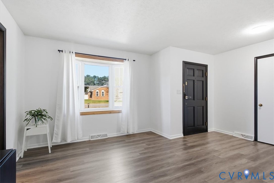 Interior space featuring wood-finish flooring, a multi-pane bay window, and a paneled entry door with contrasting trim