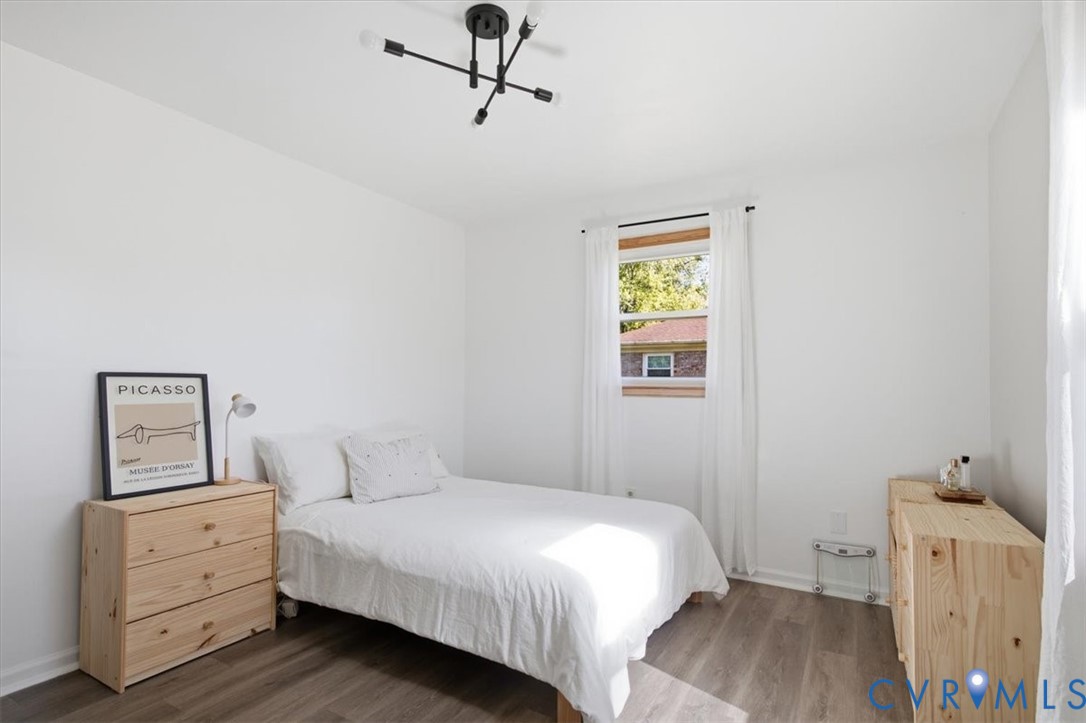 Bedroom featuring wood-finish flooring, a matte black multi-arm light fixture, and a single-hung window with a natural wood frame