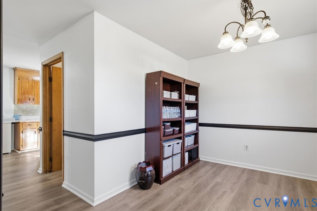 Interior space featuring wood-finish flooring, dark-toned chair rail molding, and a multi-arm chandelier with frosted glass shades