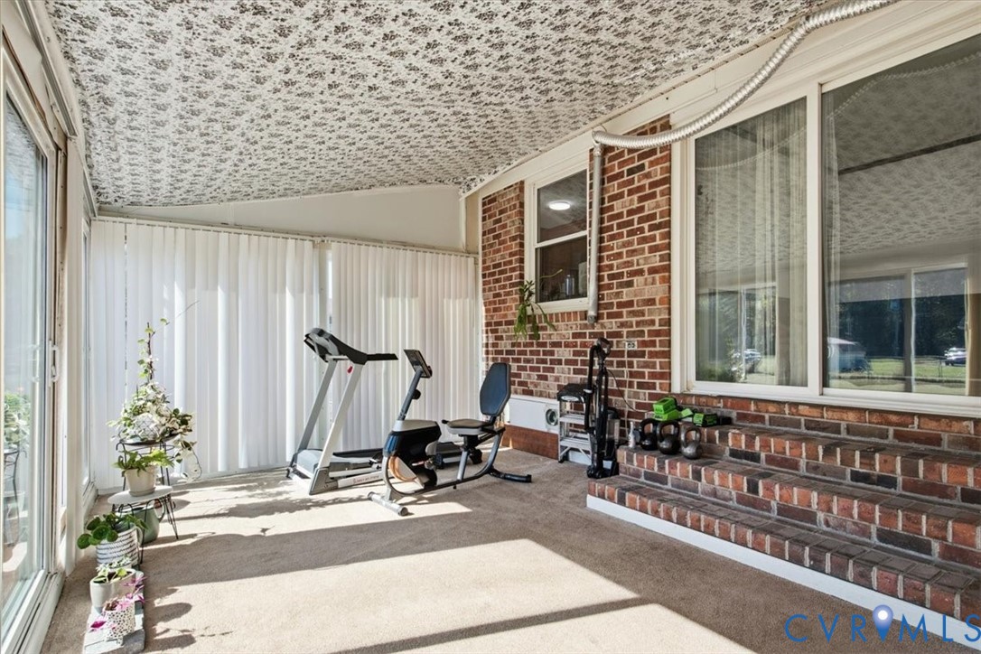 Enclosed patio featuring patterned ceiling, exposed brick wall, carpeted flooring, and multi-paneled sliding glass doors