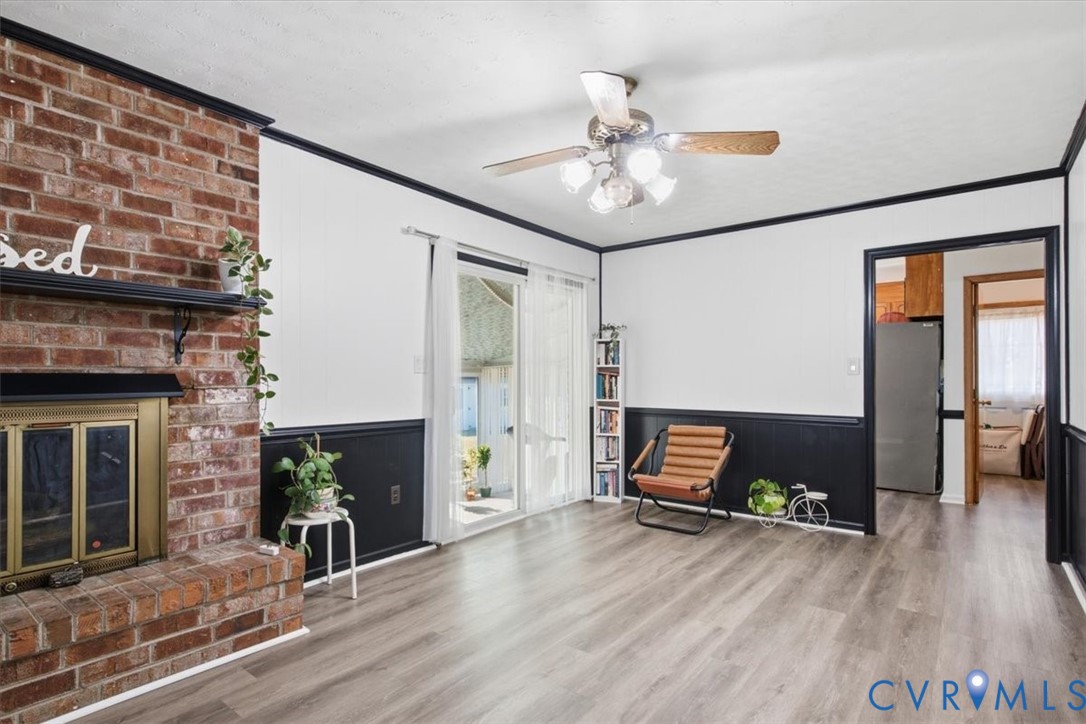 Full-height red brick fireplace featuring a metal fire screen and mantel, wood-finish flooring, dark wainscoting, sliding glass door, and a ceiling fan with multi-light fixture