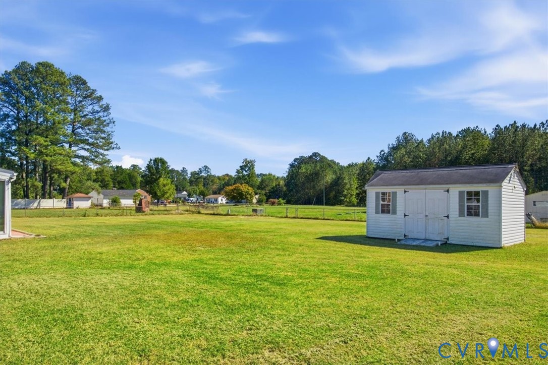 Expansive level lot featuring a grass lawn, white vinyl storage shed, perimeter fencing, and mature trees