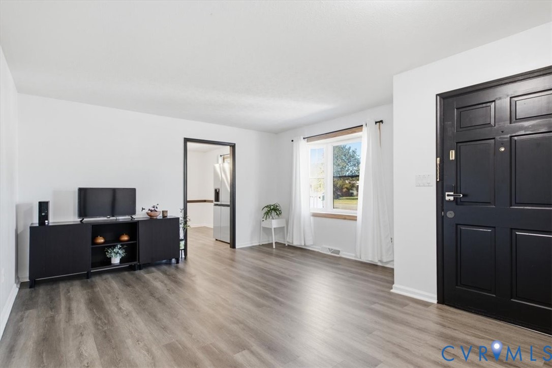 Neutral interior featuring wood-finish flooring, a matte black paneled entry door, and a multi-pane window