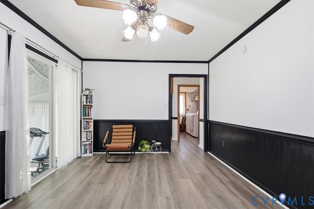 Interior space featuring wood-finish flooring, high-contrast wainscoting, crown molding, a multi-light ceiling fan, and a sliding glass door