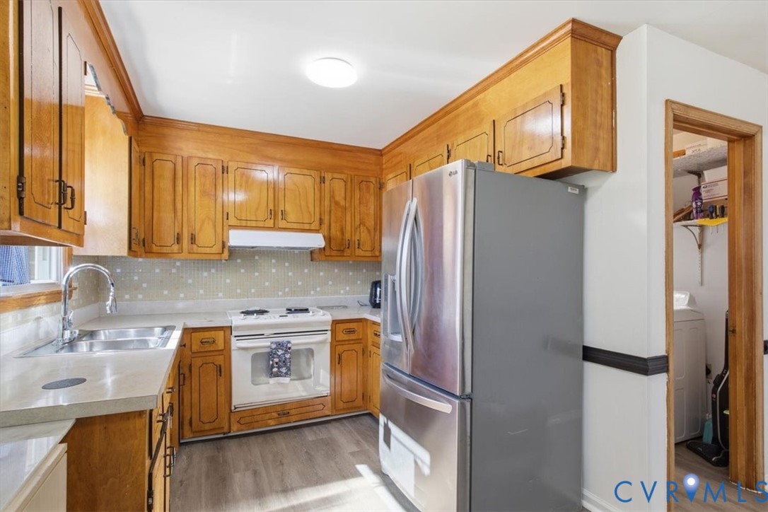 Kitchen featuring wood cabinetry, stainless steel refrigerator, white electric range, integrated backsplash, and wood-finish flooring