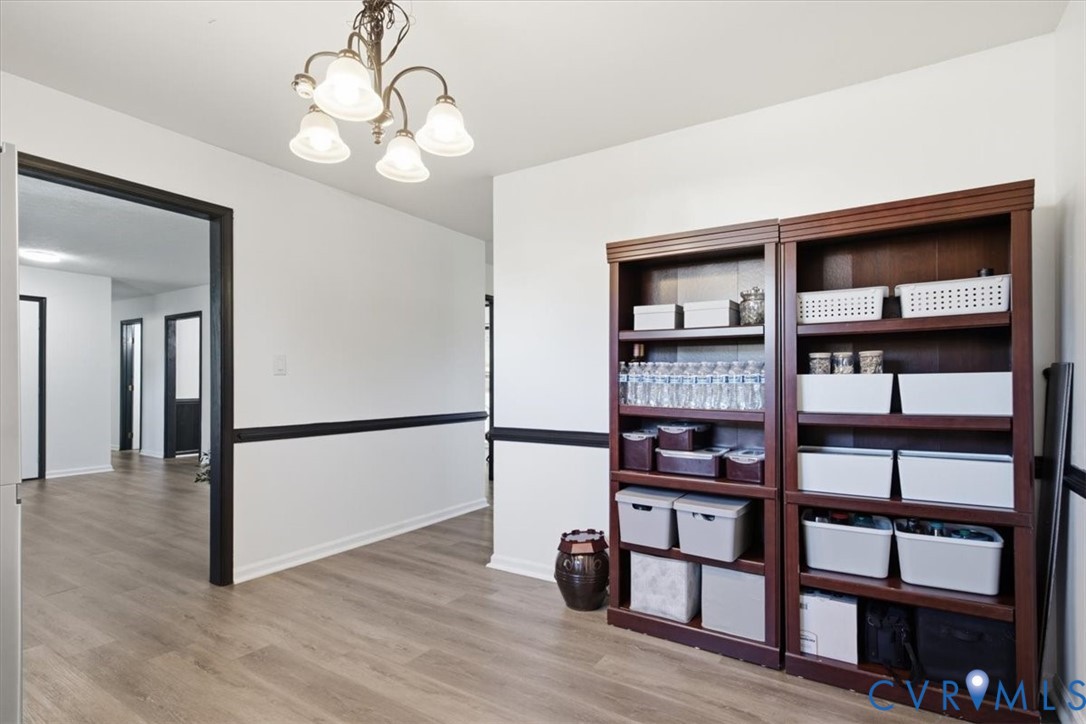 Wood-finish flooring, dark-toned crown molding and door casings, and a multi-arm chandelier with glass shades