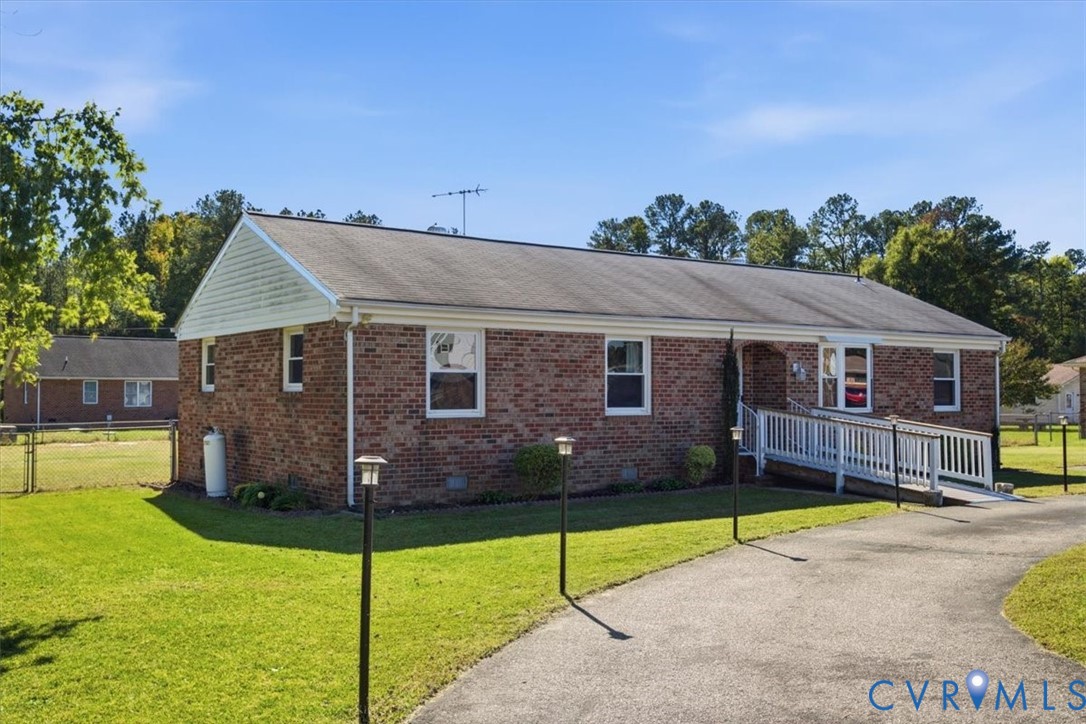 Ranch-style brick exterior featuring a gable roof, vinyl siding accents, and a paved driveway with an integrated wheelchair-accessible ramp Ranch-style brick exterior featuring a gable roof, vinyl siding accents, and a paved driveway with an integrated wheelchair-accessible ramp