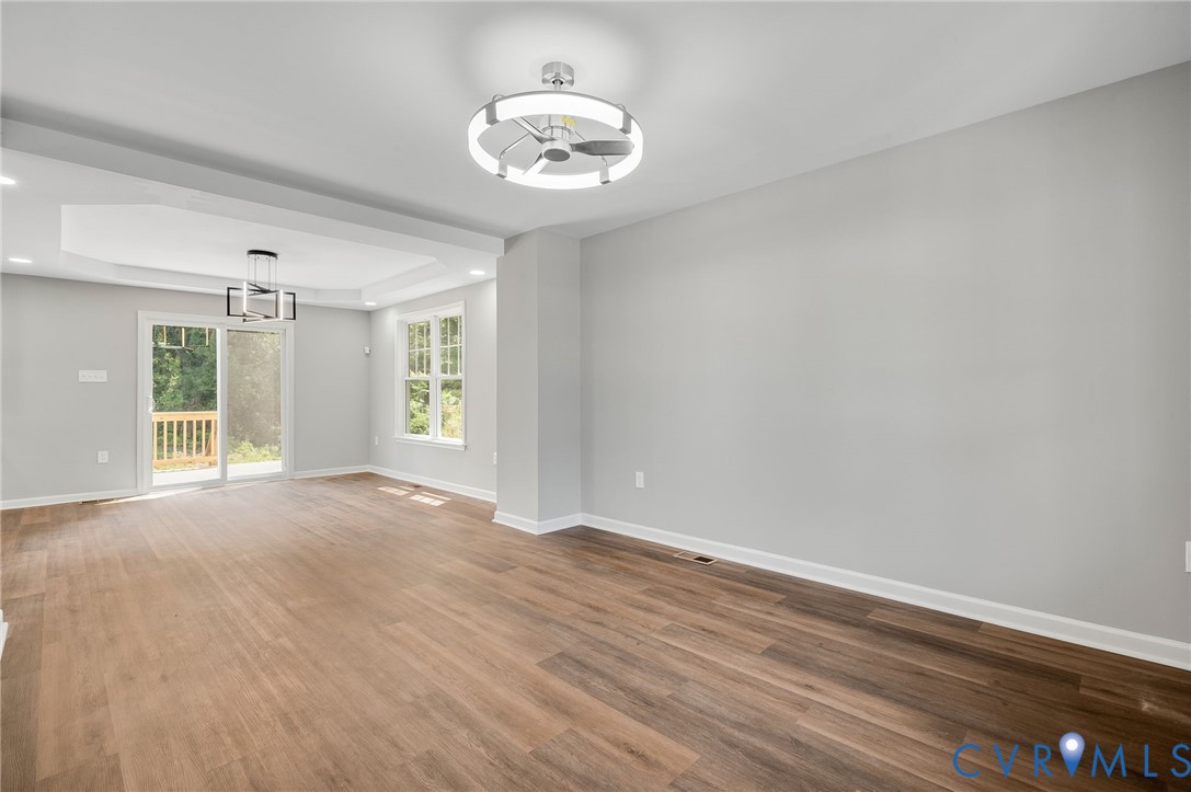 Open-concept area featuring wood-finish flooring, a tray ceiling, modern circular LED light fixtures, and a sliding glass door Open-concept area featuring wood-finish flooring, a tray ceiling, modern circular LED light fixtures, and a sliding glass door