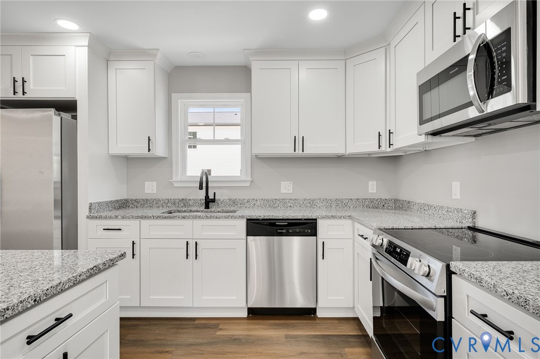 Kitchen featuring white Shaker-style cabinetry, stone-finish countertops, stainless steel appliances, matte black hardware, and wood-finish flooring