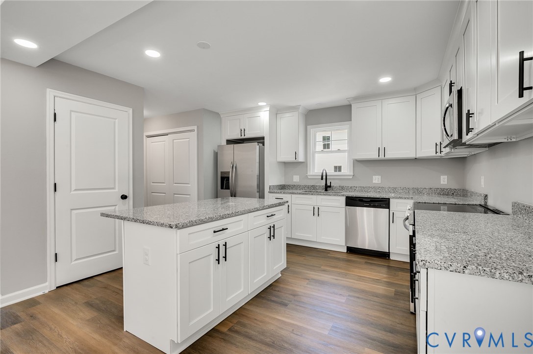 Kitchen featuring white shaker-style cabinetry, stone-finish countertops, stainless steel appliances, a center island, and wood-finish flooring