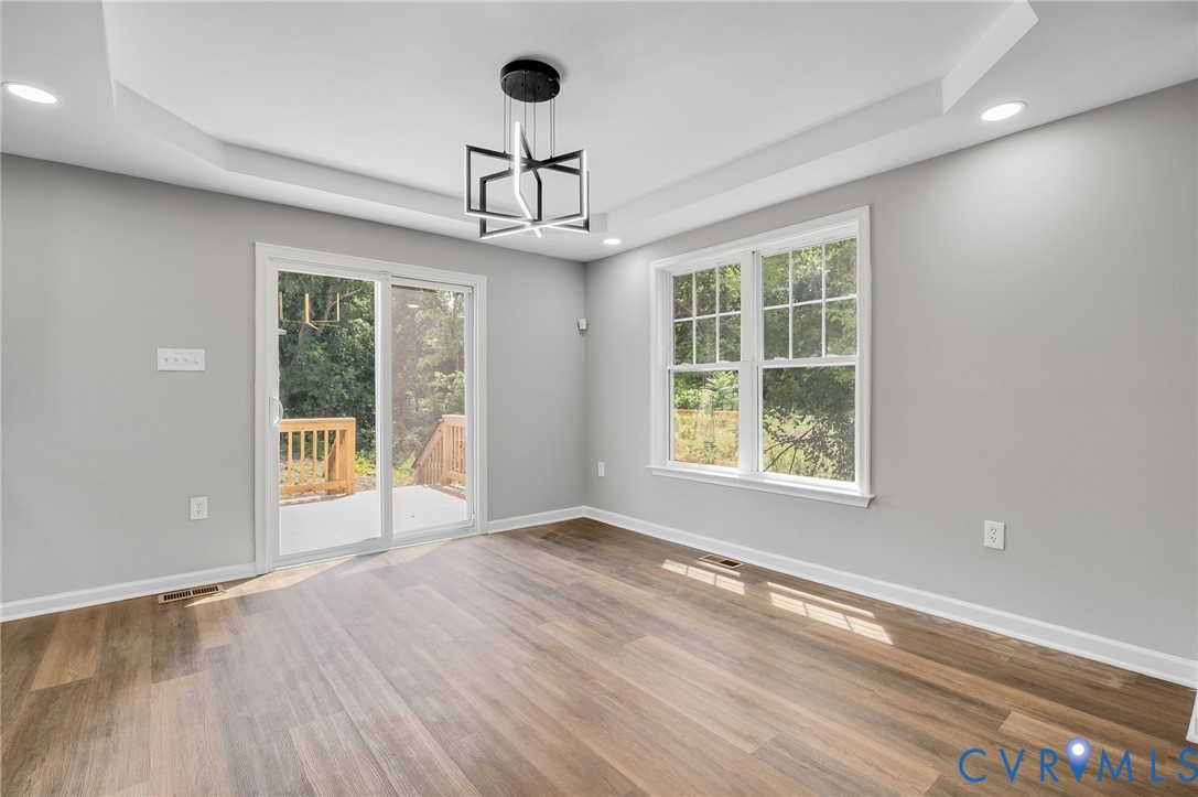 Tray ceiling featuring a geometric pendant light, wood-finish flooring, recessed lighting, and sliding glass doors Tray ceiling featuring a geometric pendant light, wood-finish flooring, recessed lighting, and sliding glass doors