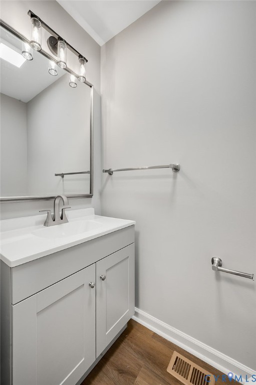 Single-sink vanity with white surface, integrated basin, grey cabinet doors, polished metal fixture, and rectangular mirror with four-light overhead vanity fixture