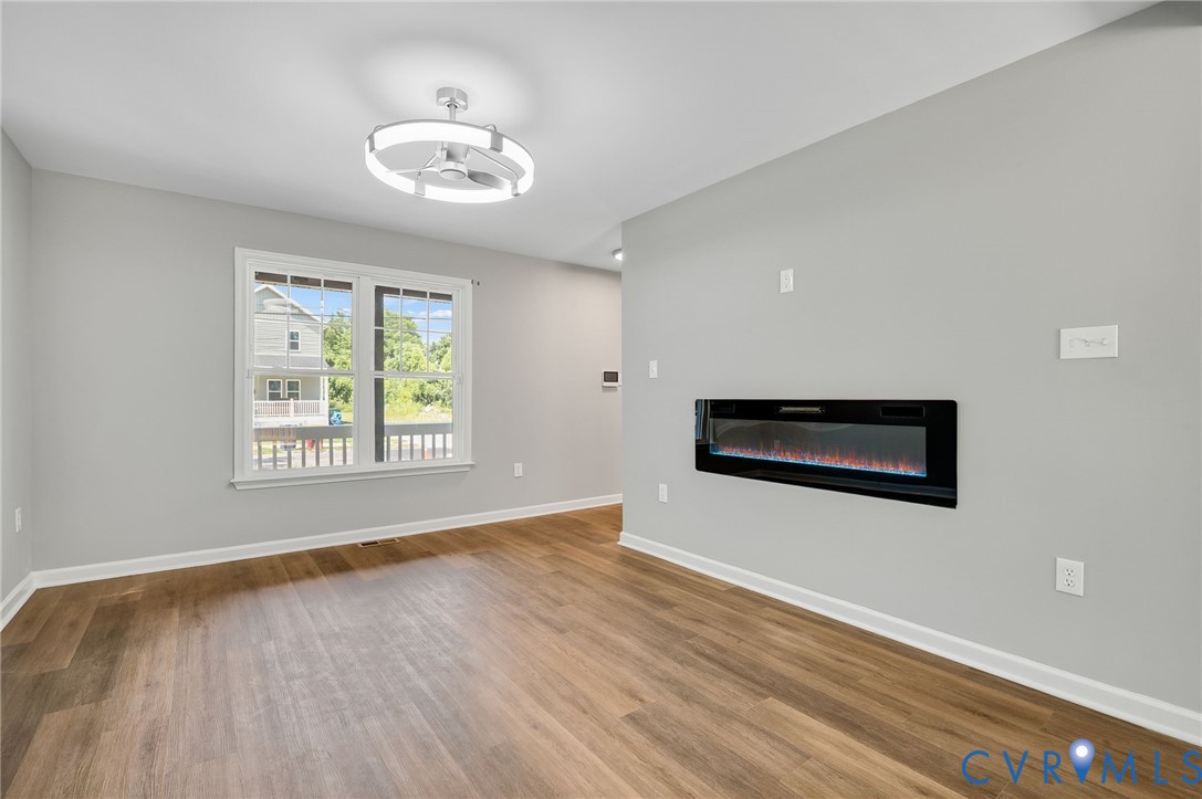 Neutral-toned interior featuring wood-finish flooring, a wall-mounted linear electric fireplace, and a contemporary circular LED ceiling fixture Neutral-toned interior featuring wood-finish flooring, a wall-mounted linear electric fireplace, and a contemporary circular LED ceiling fixture