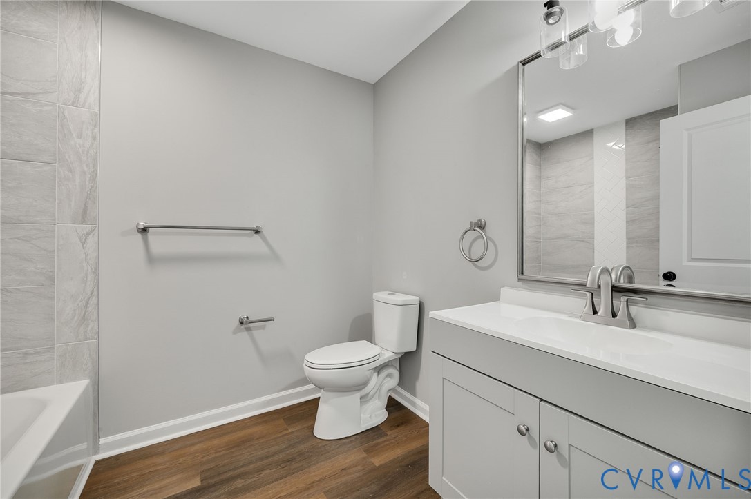 Bathroom featuring a grey vanity with a composite countertop, wood-finish flooring, a large wall-mounted mirror, and tile surround