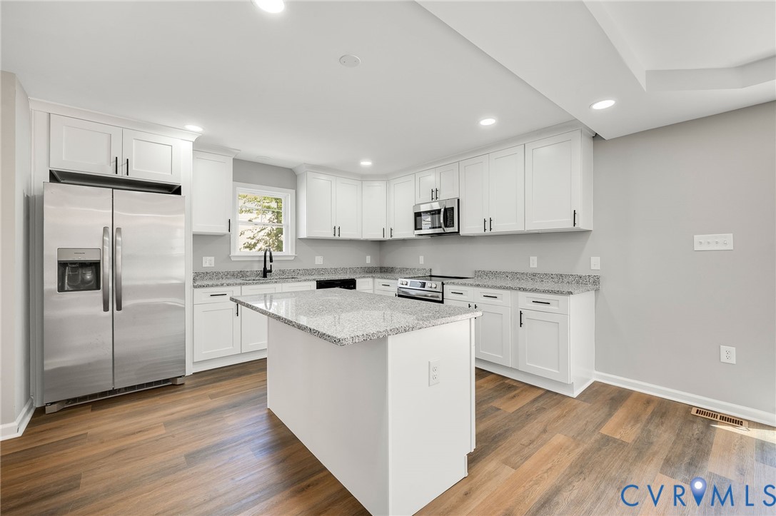 Kitchen featuring white shaker-style cabinetry, stone-finish countertops, stainless steel appliances, central island, and wood-finish flooring Kitchen featuring white shaker-style cabinetry, stone-finish countertops, stainless steel appliances, central island, and wood-finish flooring