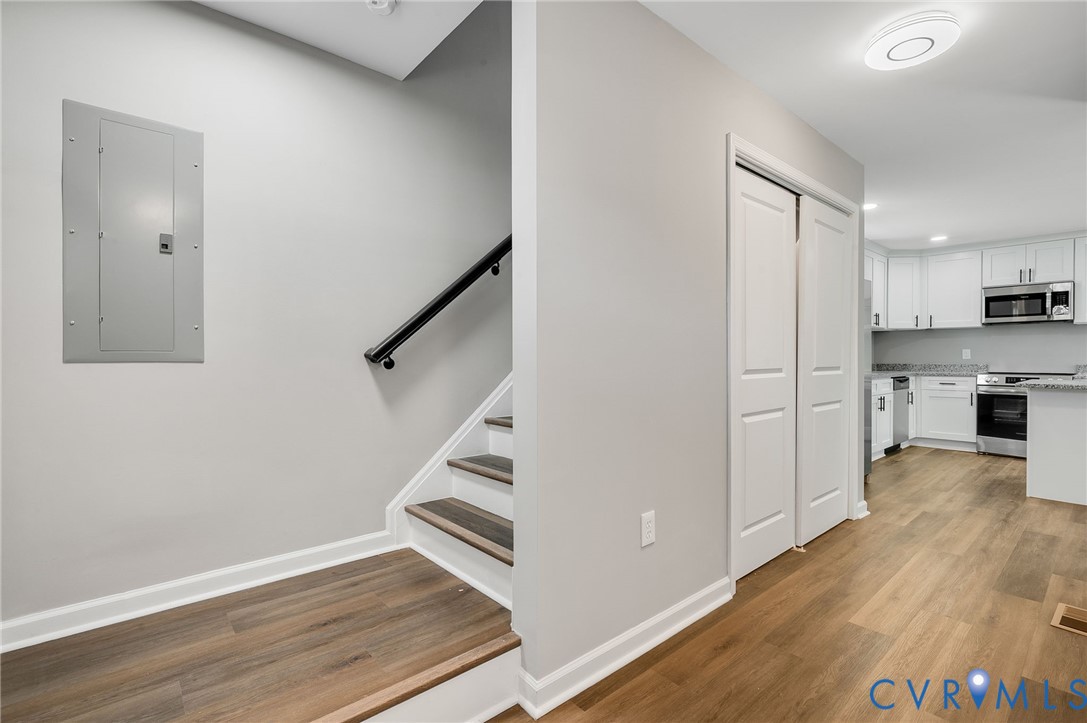 Staircase featuring wood-finish treads and a matte black handrail, wood-finish flooring, white shaker-style cabinetry, and stone-finish countertops Staircase featuring wood-finish treads and a matte black handrail, wood-finish flooring, white shaker-style cabinetry, and stone-finish countertops
