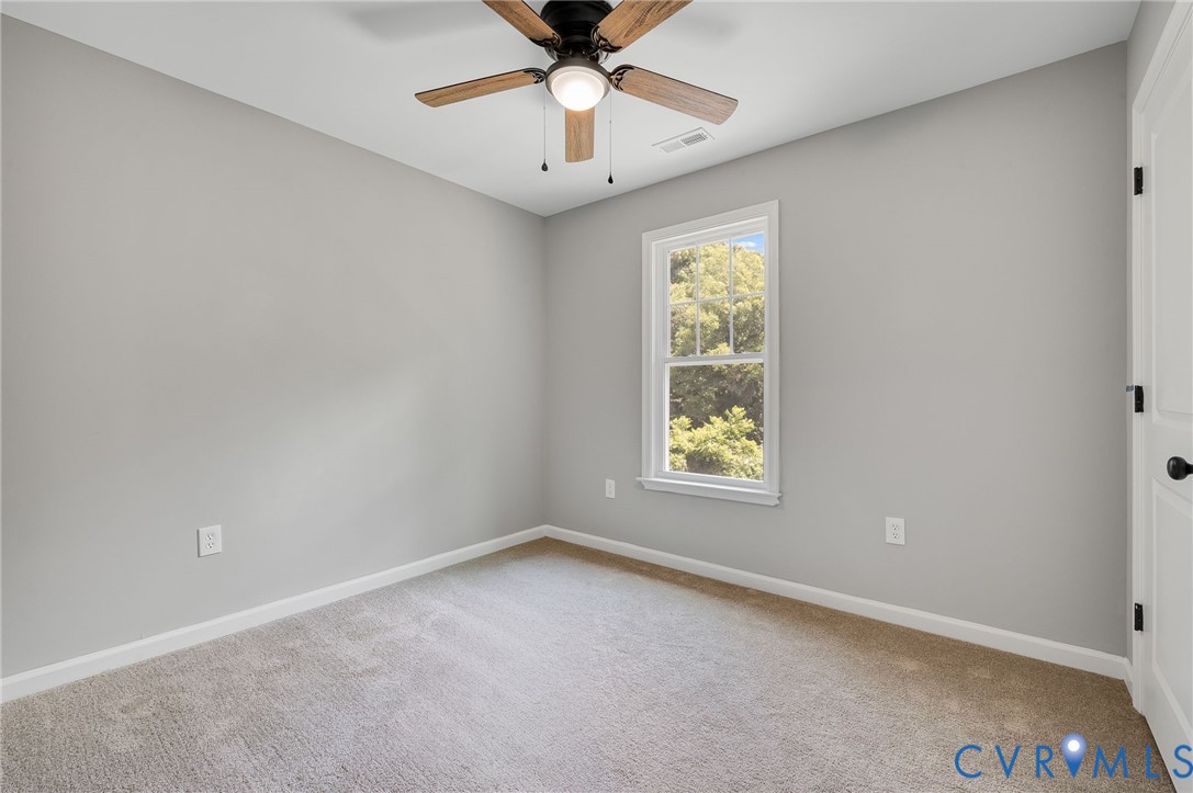 Neutral-toned interior featuring wall-to-wall carpeting, a ceiling fan with integrated lighting, and a single-hung window with exterior greenery