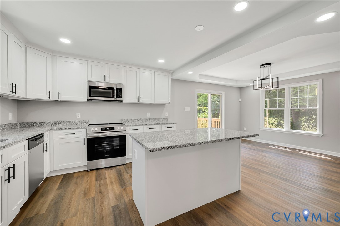 Kitchen featuring white shaker-style cabinetry, stone countertops, stainless steel appliances, a central island, and wood-finish flooring