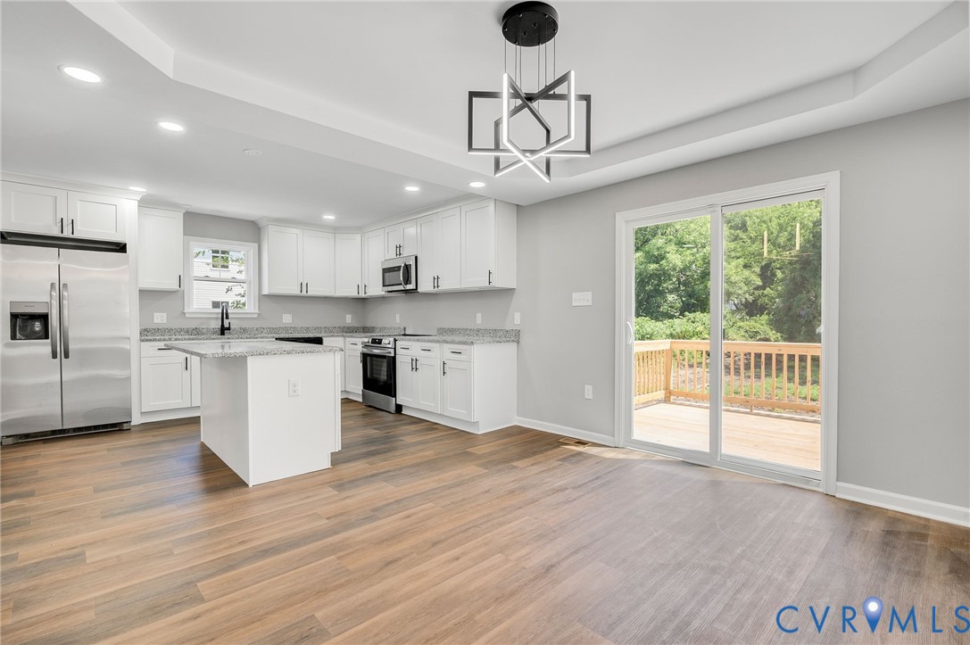 Kitchen featuring white cabinetry, stone-finish countertops, stainless steel appliances, wood-finish flooring, and a geometric chandelier Kitchen featuring white cabinetry, stone-finish countertops, stainless steel appliances, wood-finish flooring, and a geometric chandelier