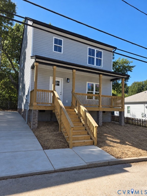Two-story residence featuring light grey horizontal siding, a covered wooden front porch with railings, and a concrete driveway Two-story residence featuring light grey horizontal siding, a covered wooden front porch with railings, and a concrete driveway