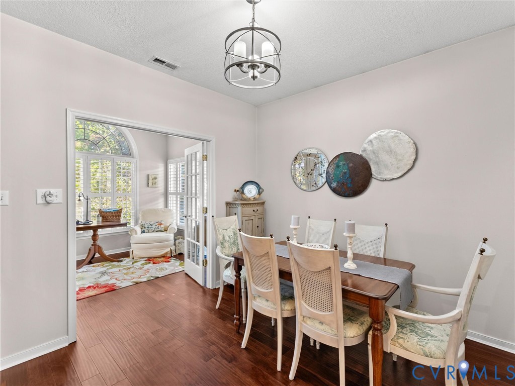 Dark wood-finish flooring, architectural glass-paned French doors, and a modern tiered geometric chandelier